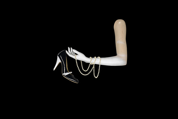 Mannequin arm holding a high-heeled shoe with a string of pearls wrapped around the arm