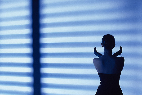 Blue light of a shadow from a Venetian blind cast onto a woman with her back to the camera